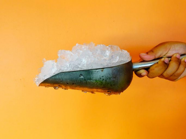 photo of a hand holding a metal scoop filled with ice in front of a yellow background